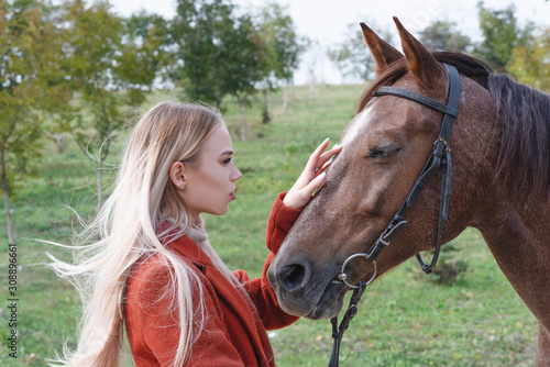 A beautiful, young, stylish girl stands next to a horse next to the road. © Валентина Баранова