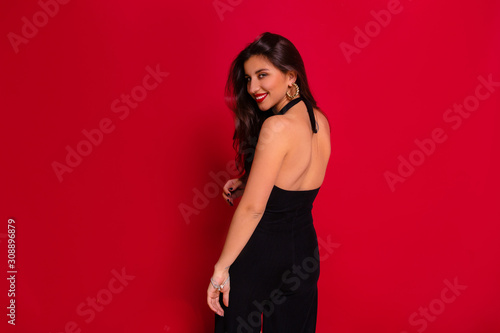 Studio portrait of elegant charming woman wearing black dress with bare back posing at camera over red background