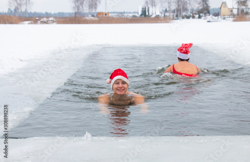 two girls in santa hat swim ice-hole in frost in winter