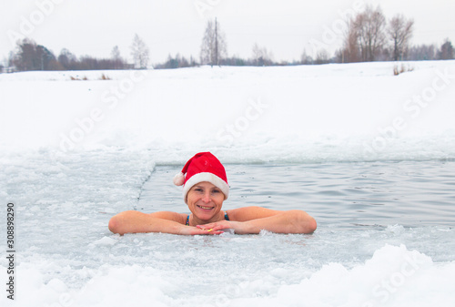 woman in santa claus hat is swimming extreme ice hole in frost in winter © Inga
