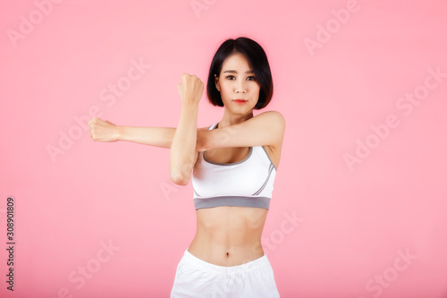 Young sporty woman doing shoulder and arm stretching isolated on pink background. © skarie