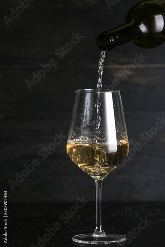 Fotografie Pouring of tasty wine into glass against dark background