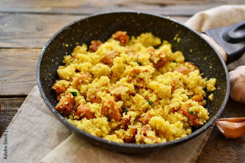 Couscous in a pan on a wooden background. Couscous with pieces of chicken in a pan. Couscous in a pan on a wooden background. Couscous with pieces of chicken in a pan.