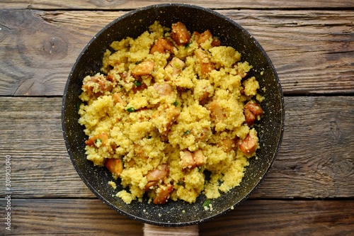 Couscous in a pan on a wooden background. Couscous with pieces of chicken in a pan.