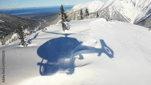 Actionsportlers were dropped by a helicopter at the top of the mountains. The sun is shining brightly in the blue sky. There is a mountain range in the background covered in snow. Drone shooting. photo