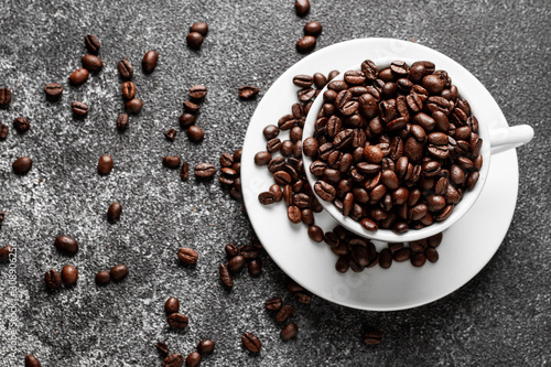 Roasted coffee beans in white cup. Dark concrete background. Top view.