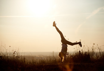 Young girl doing a handstand. Beautiful view horizon of a sunset on the background