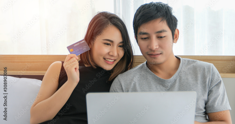 Asian Couple shopping online and paying with credit card at laptop computer,Happy couple at home surfing the net in bed Asian Couple shopping online and paying with credit card at laptop computer,Happy couple at home surfing the net in bed