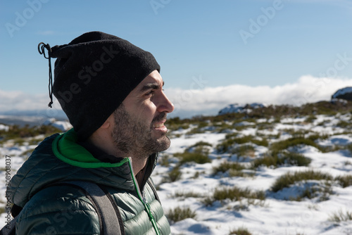YOUNG CAUCASIAN MAN EQUIPPED WITH MOUNTAIN CLOTHES ENJOYING A TREKING WALK IN SNOWY LANDSCAPE WITH BLUE SKY AND SUNSHINE