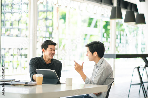 Young Asian businessmen using a digital tablet to discuss information in a modern business working space.
