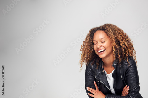Studio Shot Of Happy Young Woman With Folded Arms Wearing Leather Jacket Laughing Off Camera photo