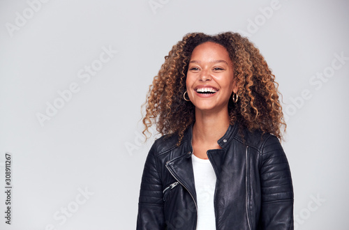 Waist Up Studio Shot Of Happy Young Woman Wearing Leather Jacket Laughing Off Camera photo
