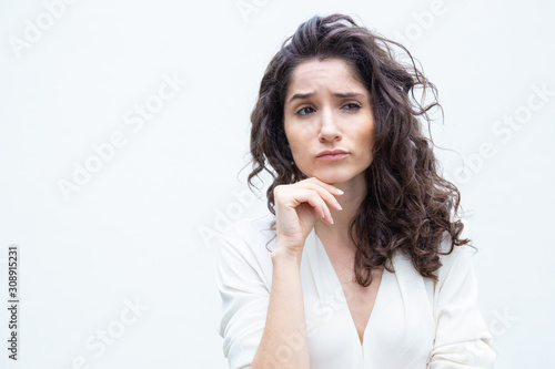 Thoughtful female customer leaning chin on hand, looking away. Wavy haired young woman in casual shirt standing isolated over white background. Pensive woman or advertising concept