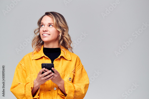 Studio Shot Of Causally Dressed Young Woman Using Mobile Phone Looking Off Camera photo