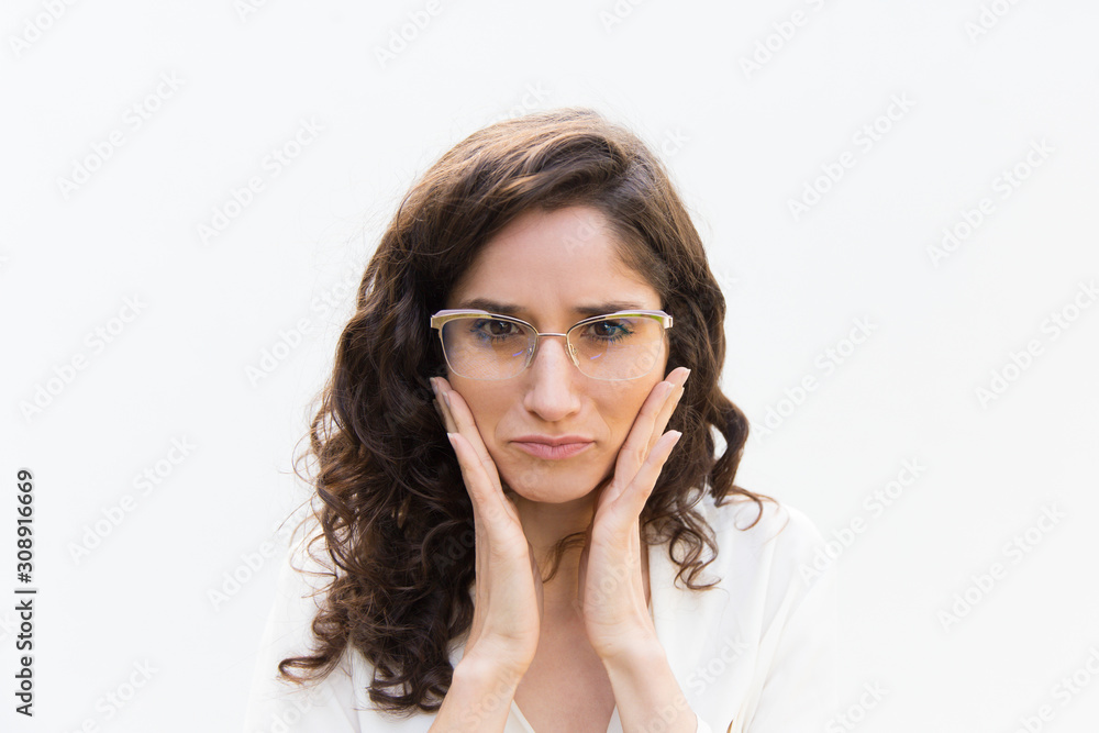 Serious strict female office worker wearing glasses, touching facial skin. Wavy haired young woman in casual shirt standing isolated over white background. Skin care concept Serious strict female office worker wearing glasses, touching facial skin. Wavy haired young woman in casual shirt standing isolated over white background. Skin care concept