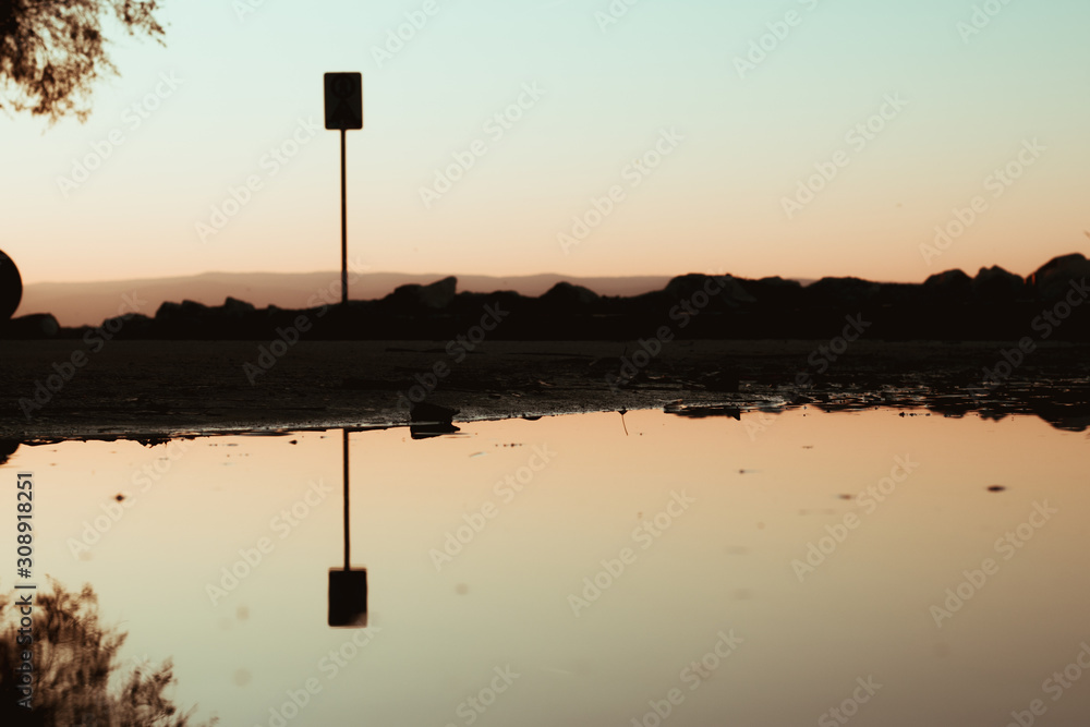 Dark image of a reflection in the puddle, moody dark orange picture with a silhouette of rocks and a sign