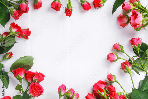 Small bright red roses on the white wooden table arraged into a frame