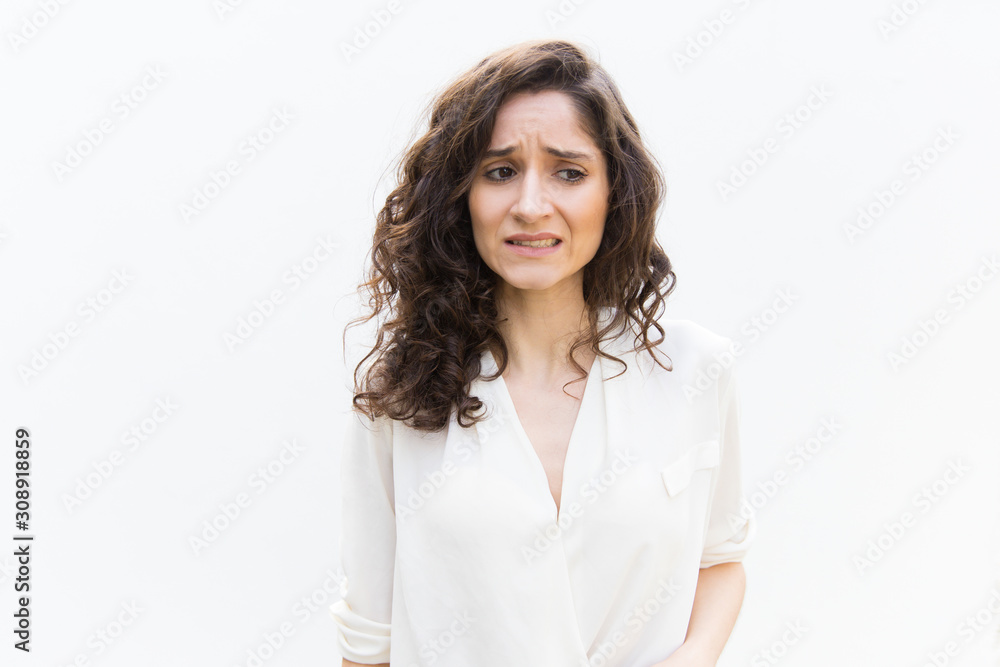 Upset woman realizing mistake, feeling guilty, looking away. Wavy haired young woman in casual shirt standing isolated over white background. Stress or error concept Upset woman realizing mistake, feeling guilty, looking away. Wavy haired young woman in casual shirt standing isolated over white background. Stress or error concept
