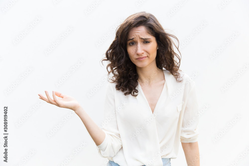Doubtful woman pointing hand at empty copy space and shrugging. Wavy haired young woman in casual shirt standing isolated over white background. Advertising concept Doubtful woman pointing hand at empty copy space and shrugging. Wavy haired young woman in casual shirt standing isolated over white background. Advertising concept