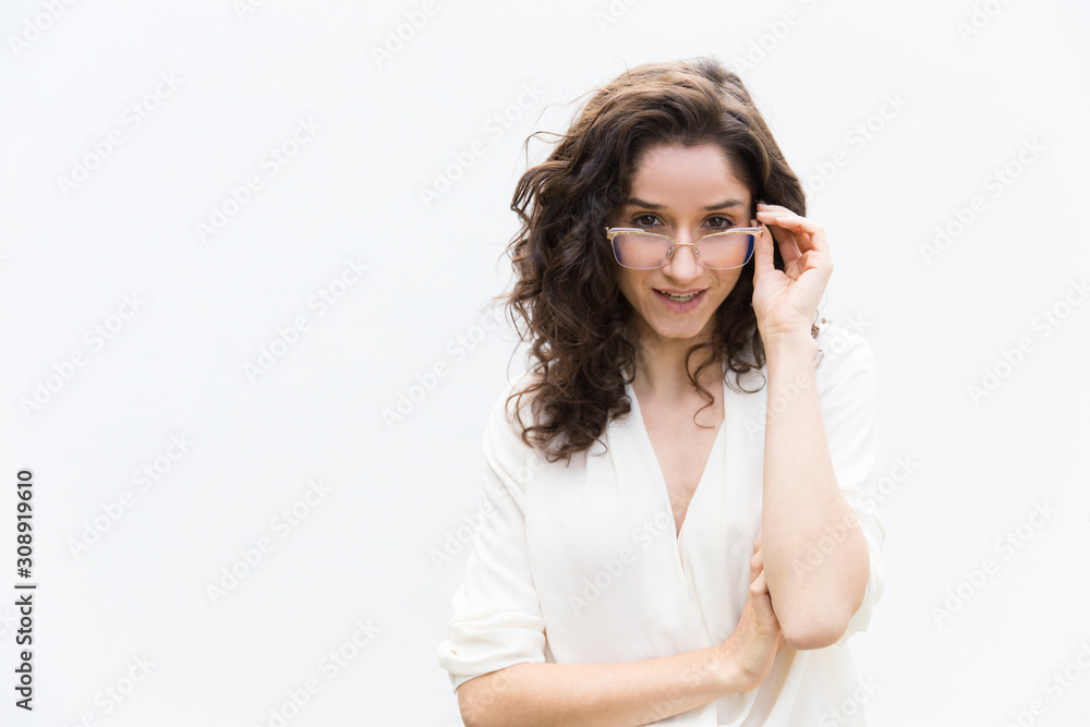 Cheerful female professional adjusting glasses, looking at camera. Wavy haired young woman in casual shirt standing isolated over white background. Advertising concept Cheerful female professional adjusting glasses, looking at camera. Wavy haired young woman in casual shirt standing isolated over white background. Advertising concept