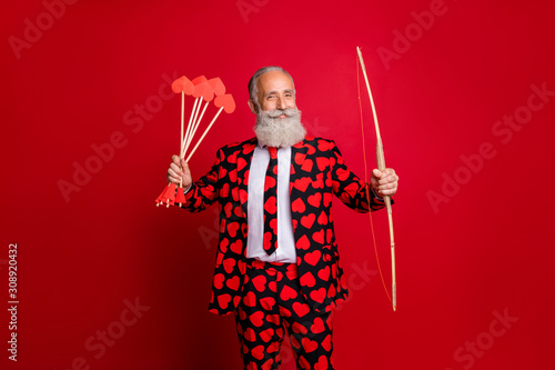 Photo of crazy cupid mature handsome guy valentine day hold bow arrow ready to shoot loving couple wear hearts pattern stylish suit tie trousers blazer isolated red color background photo