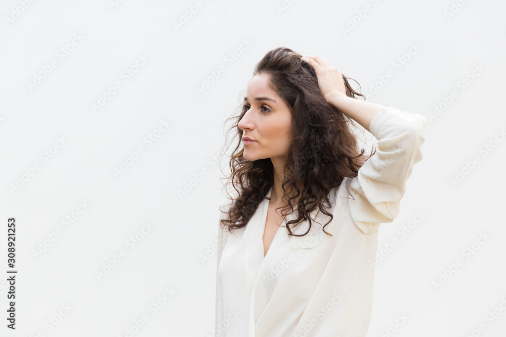 Side of pensive serious beautiful woman touching hair and looking away at copy space. Wavy haired young woman in casual shirt standing isolated over white background. Advertising concept Side of pensive serious beautiful woman touching hair and looking away at copy space. Wavy haired young woman in casual shirt standing isolated over white background. Advertising concept