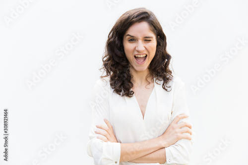 Joyful amazed student girl winking at camera. Wavy haired young woman in casual shirt standing isolated over white background. Positive emotion concept © Mangostar