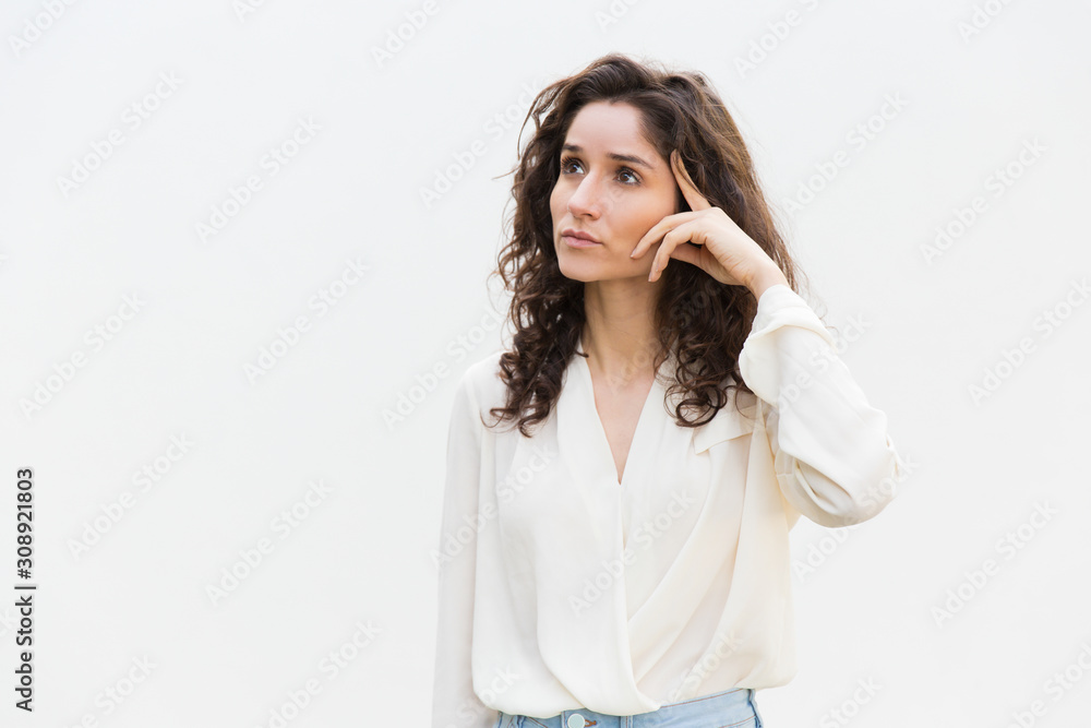 Pensive woman touching head and looking up at copy space. Wavy haired young woman in casual shirt standing isolated over white background. Promotion concept Pensive woman touching head and looking up at copy space. Wavy haired young woman in casual shirt standing isolated over white background. Promotion concept