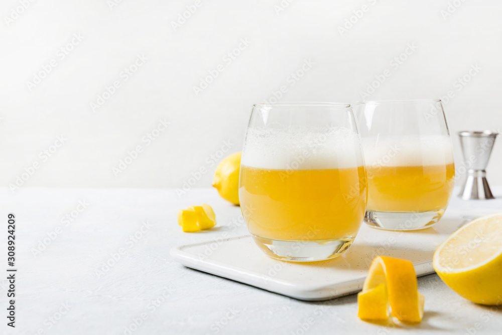 Two whiskey sour cocktails with ingredients, lemon juice, sugar syrup and egg white in glass on white. Horizontal orientation. Two whiskey sour cocktails with ingredients, lemon juice, sugar syrup and egg white in glass on white. Horizontal orientation.