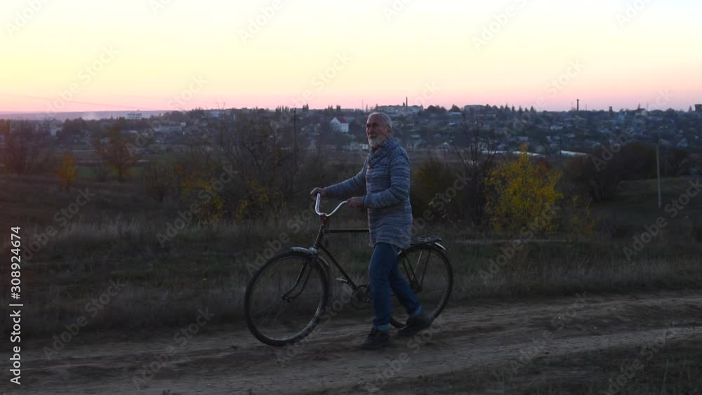 Old man with a gray hair and beard walking with a bicycle along road, rustic style Old man with a gray hair and beard walking with a bicycle along road, rustic style