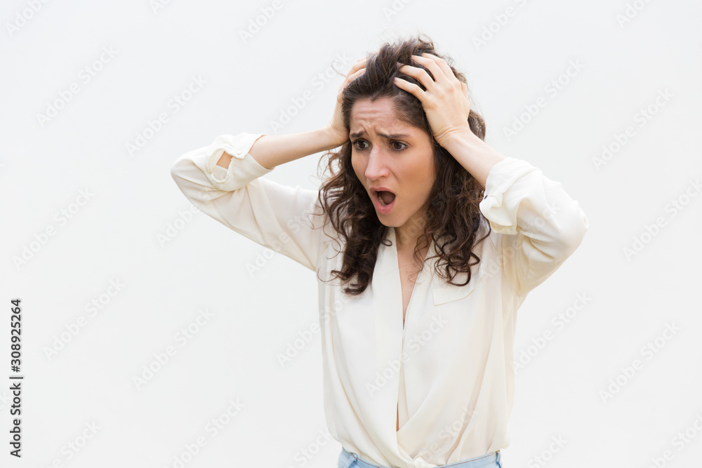 Shocked disappointed woman gasping, holding head and staring away at copy space. Wavy haired young woman in casual shirt standing isolated over white background. Mistake or stress concept Shocked disappointed woman gasping, holding head and staring away at copy space. Wavy haired young woman in casual shirt standing isolated over white background. Mistake or stress concept