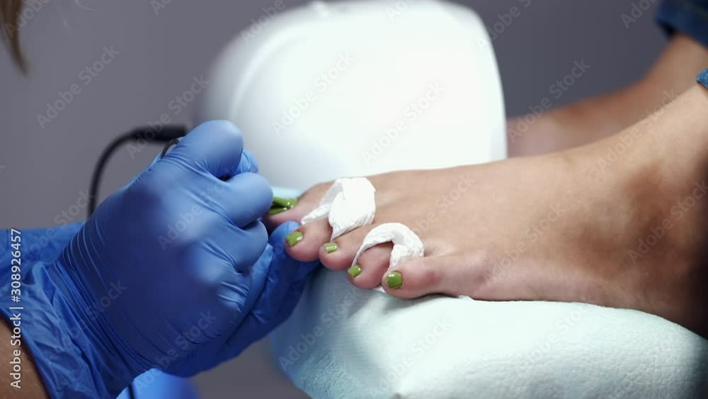 The toes are separated. The master is applying the green nail polish. The pedicure technician is