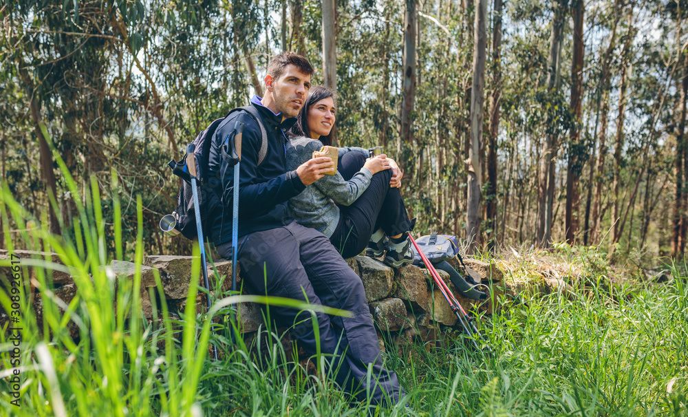 Young couple pausing to eat and drink while doing trekking outdoors enjoying nature Young couple pausing to eat and drink while doing trekking outdoors enjoying nature