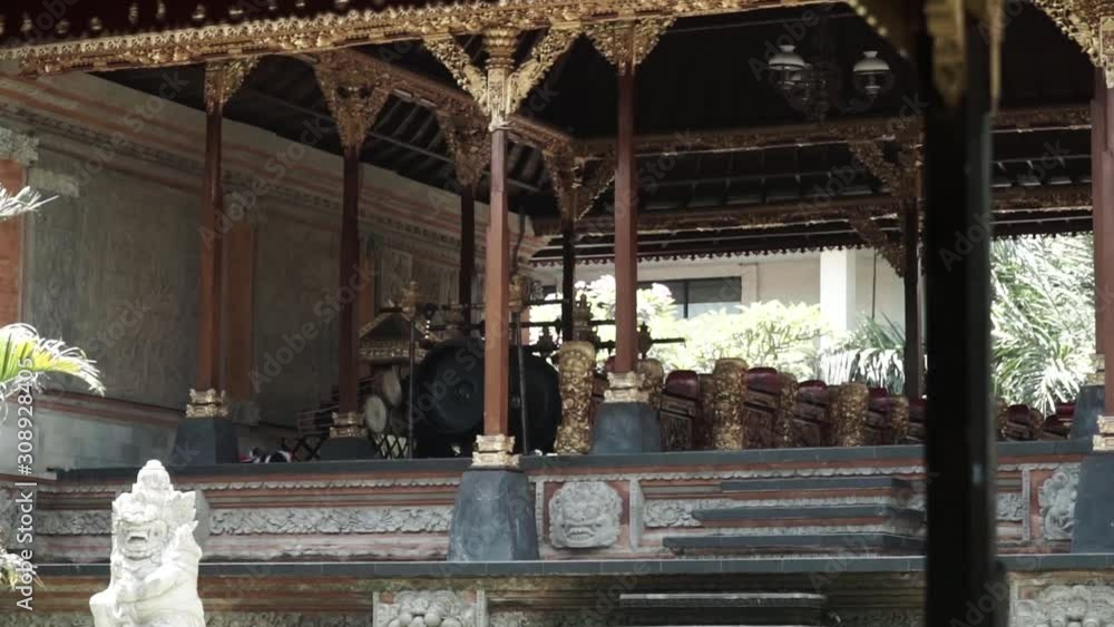 This is inside the Ubud palace in the daytime, filming handheld, the camera pans right, details like roof, gong and benches covered in gold This is inside the Ubud palace in the daytime, filming handheld, the camera pans right, details like roof, gong and benches covered in gold