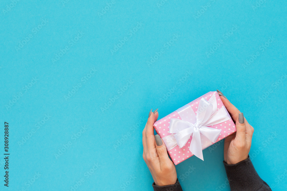 Girl holds gift box, pink gift box in polka dots with white ribbon and bow on a blue background , flat lay, top view, birthday or valentines day Girl holds gift box, pink gift box in polka dots with white ribbon and bow on a blue background , flat lay, top view, birthday or valentines day