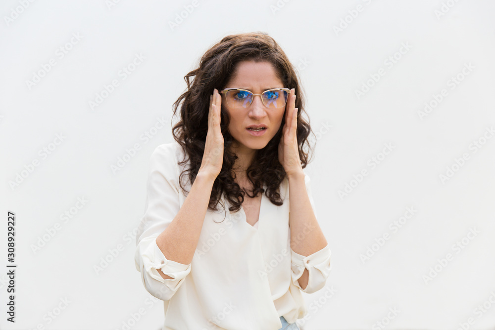 Suspicious worried woman adjusting glasses and staring at camera. Wavy haired young woman in casual shirt standing isolated over white background. Concern concept Suspicious worried woman adjusting glasses and staring at camera. Wavy haired young woman in casual shirt standing isolated over white background. Concern concept