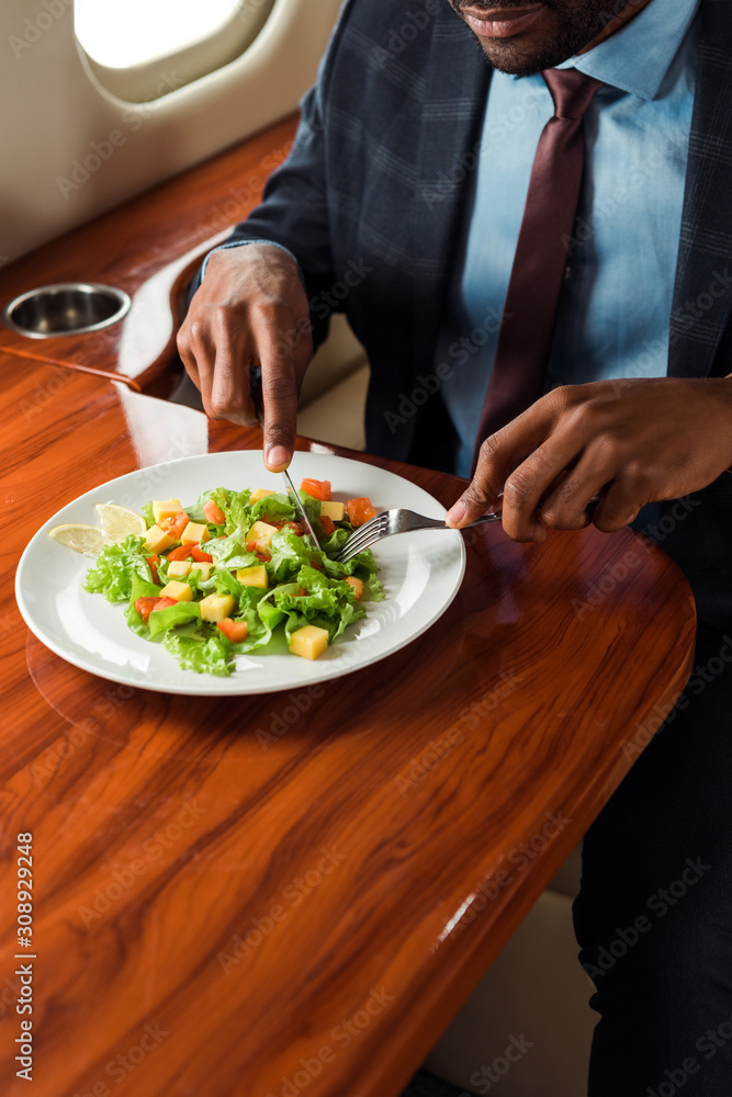 Φωτογραφία cropped view of african american businessman holding cutlery near salad in priva