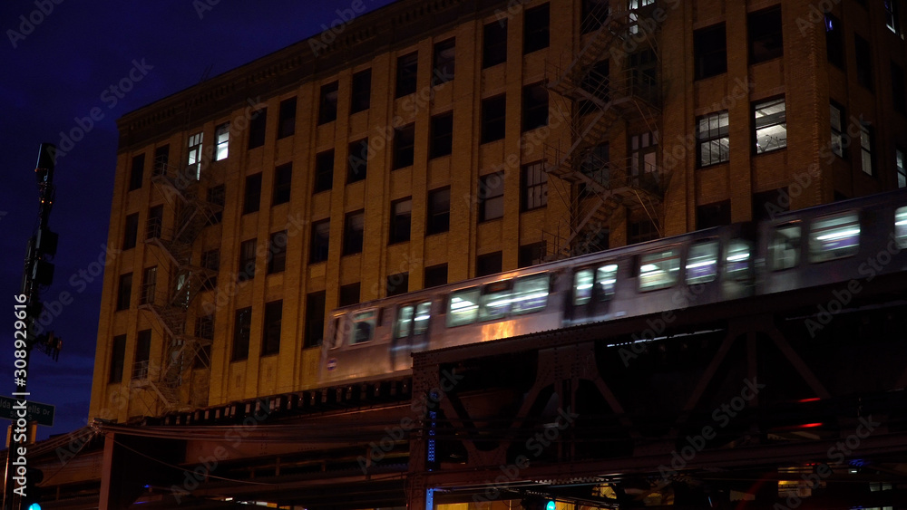 Chicago loop train passing by downtown apartment building at night on overhead elevated track through city. Public transportation to city nightlife