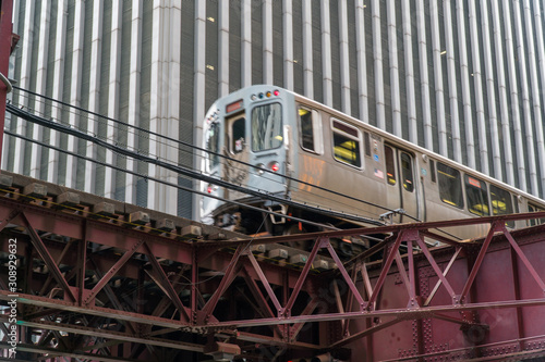 Day time establishing shot of Chicago L train passing by downtown office building on tracks elevated overhead roadway.