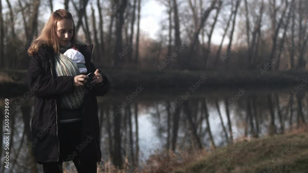 Mother takes selfie by lake on a walk with baby in pouch, full