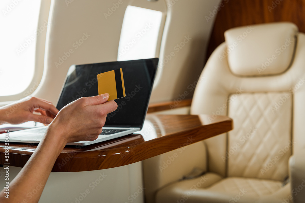 cropped view of businesswoman holding credit card near laptop in private plane cropped view of businesswoman holding credit card near laptop in private plane