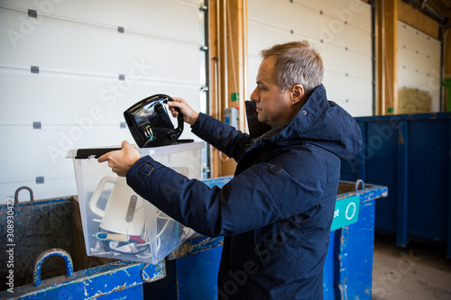 Fotografie A man putting old appliances into dumpster in sorting centre for safe disposal a