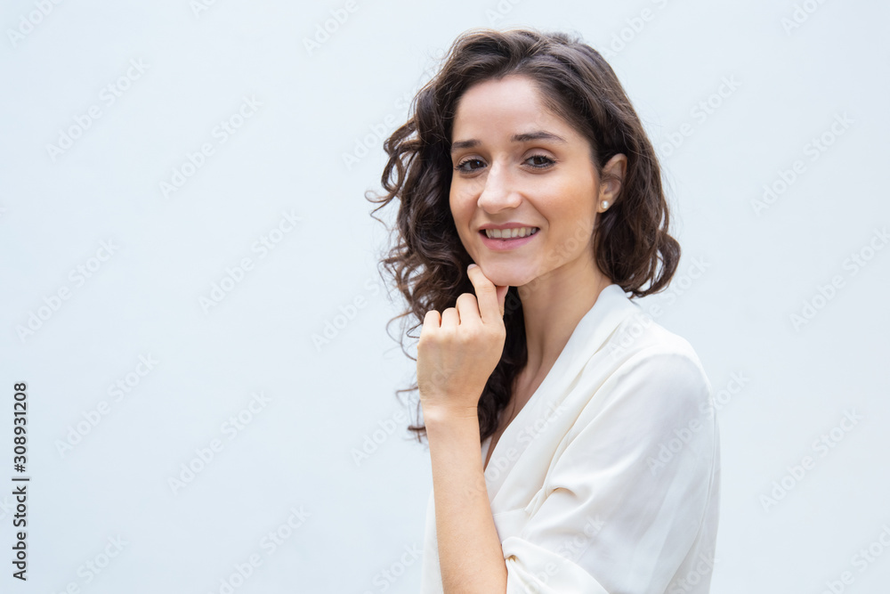 Happy pensive attractive student girl touching chin, turning face to camera, smiling. Wavy haired young woman in casual shirt standing isolated over white background. Female portrait concept Happy pensive attractive student girl touching chin, turning face to camera, smiling. Wavy haired young woman in casual shirt standing isolated over white background. Female portrait concept
