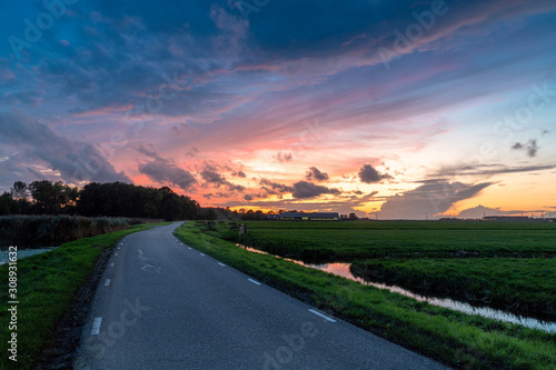 Road to sunset in Hazerswoude Rijndijk, the Netherlands. Country road during colourful sunset. Reflection in the small canals. Dutch meadows. photo