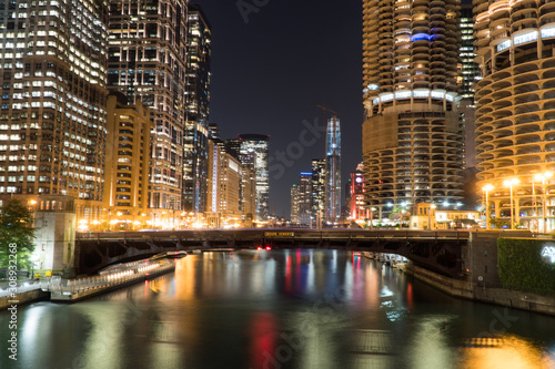 Night time exterior establishing shot overlooking Chicago river front area with skyline illuminated in dark sky reflecting off water in beautiful scene bridge road overpass with car traffic