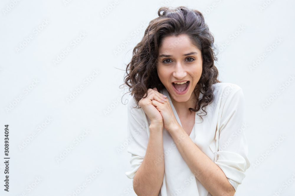 Excited overjoyed woman with clasped hands gasping or shouting for joy. Wavy haired young woman in casual shirt standing isolated over white background. Surprise concept Excited overjoyed woman with clasped hands gasping or shouting for joy. Wavy haired young woman in casual shirt standing isolated over white background. Surprise concept