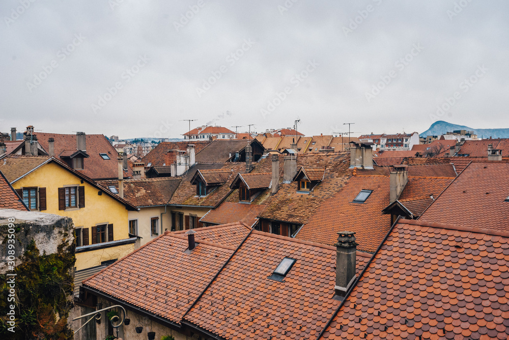 Cityscape of the roofs of European small houses in Annecy, France. Photography of the roofs covered with red tiles in the Mediterranean city against a cloudy sky on the mountains background.