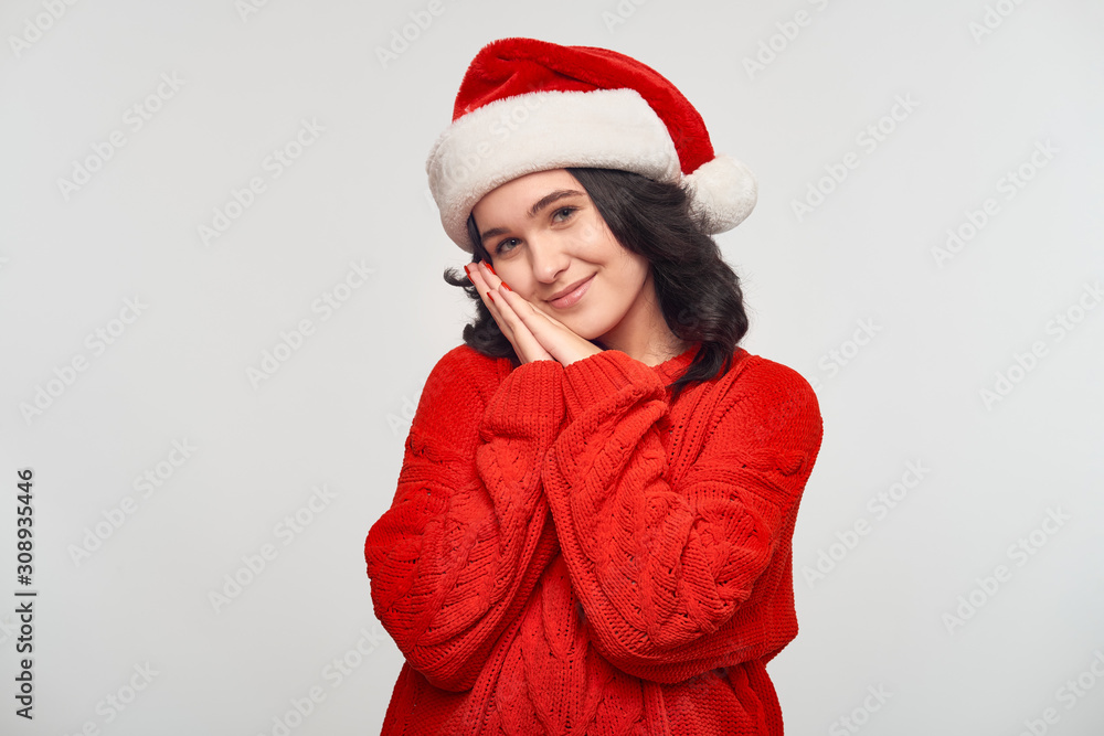 Pretty brunette girl in a red sweater and Santa hat isolated over grey background. Pretty brunette girl in a red sweater and Santa hat isolated over grey background.