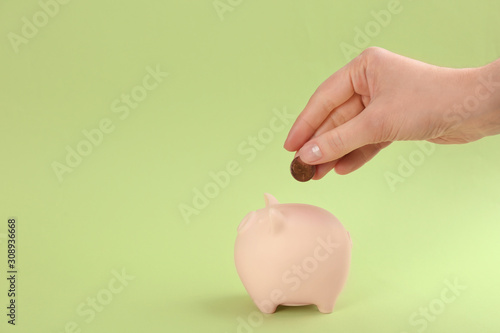 Woman putting coin into piggy bank on green background, closeup photo