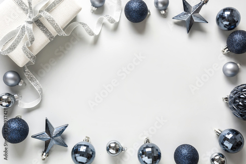 Christmas frame of classic blue balls and gift box on neutral pastel grey. Top view. Xmas border for wishes. Holiday greeting card.